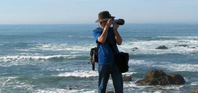 a man standing on top of a lush green hillside next to the ocean by Simon Hurry courtesy of Unsplash.